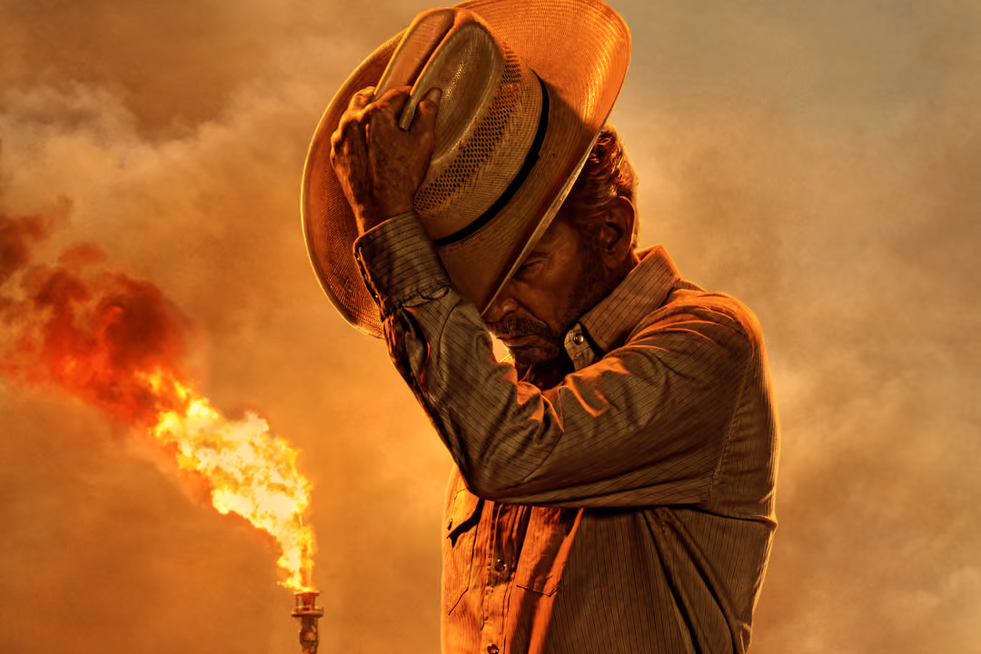 Man holding a cowboy hat against a smoky orange sky with flames in background.